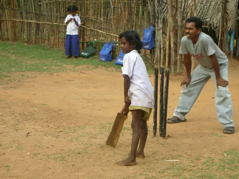 A girl batting in front of the stumps on a village ground.