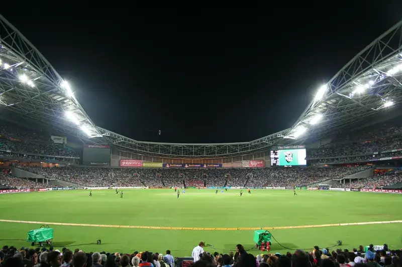 A floodlit cricket stadium during a night match.