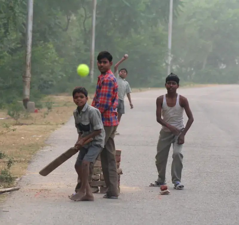 Boys playing cricket on a village road, the ball in the air.